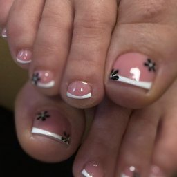 JOWIN JOANNA WINKIEL - Zbliżenie na stopy z precyzyjnym pedicure: różowa baza, białe końcówki i czarne kwiatowe zdobienia na paznokciach u stóp. Estetyczne i zadbane.