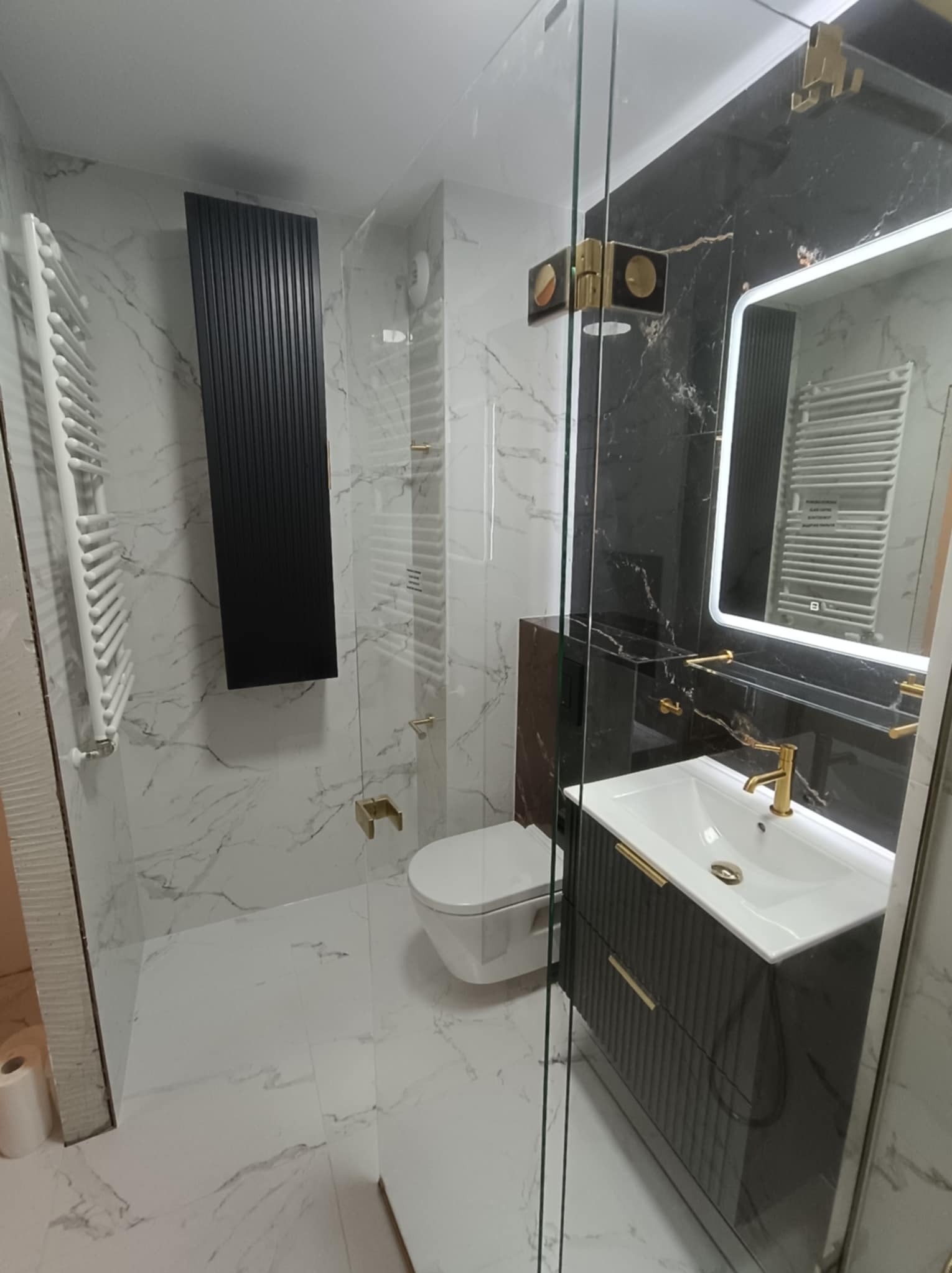 Elegancka łazienka po remoncie: marmurowe płytki, czarne akcenty, złota armatura i kabina prysznicowa ze szkła hartowanego. Nowoczesny design z dbałością o detale.
