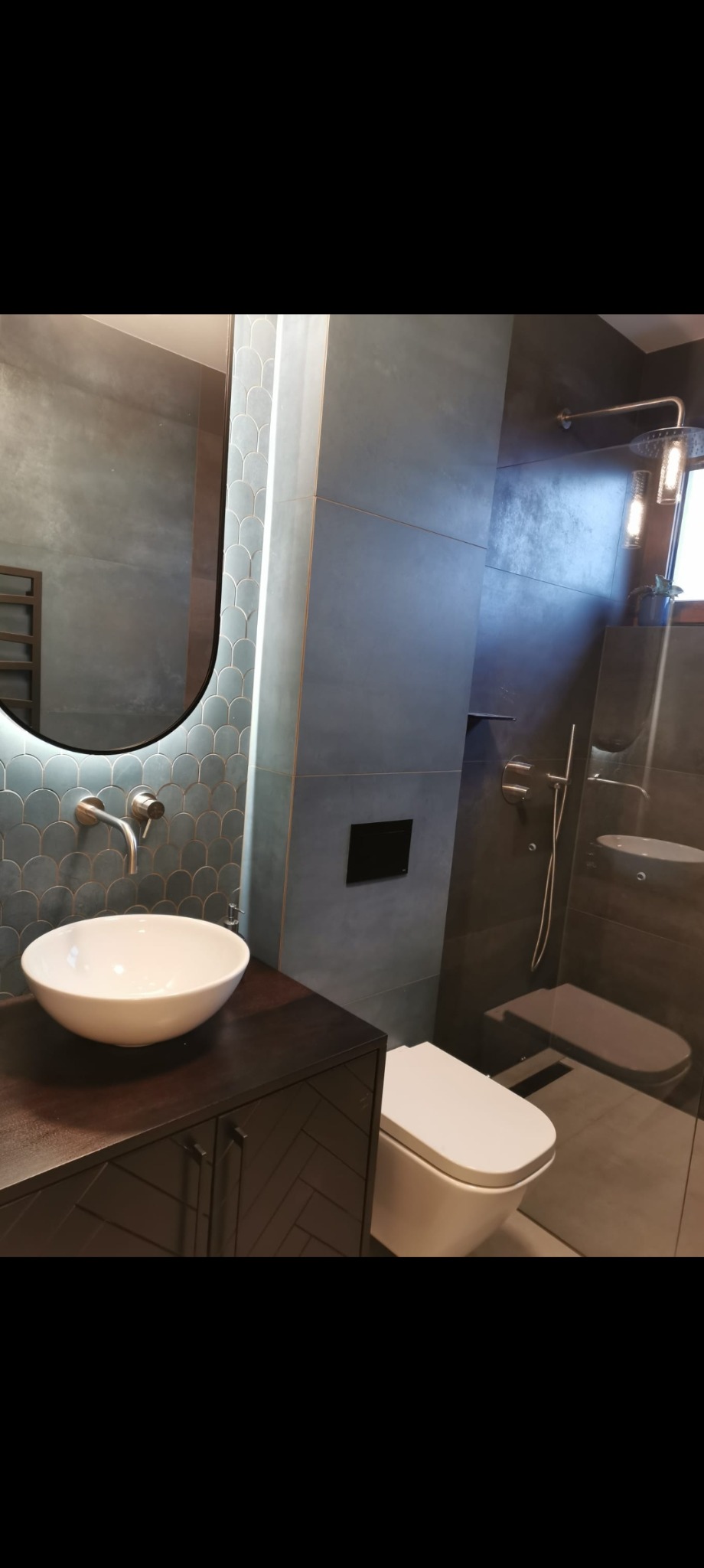 Stylowa łazienka po remoncie: umywalka nablatowa, lustro z podświetleniem LED, szare płytki i kabina prysznicowa ze szklanymi drzwiami.