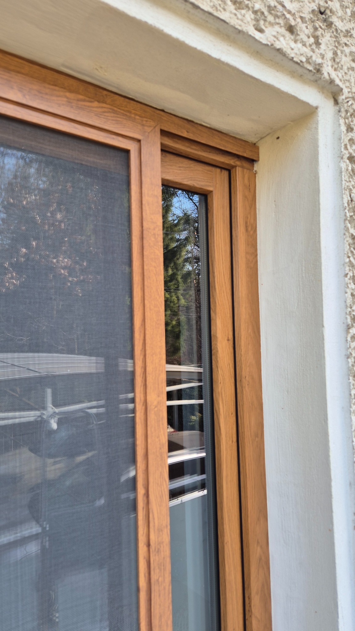 Brązowa moskitiera przesuwna na oknie, widok z zewnątrz, siatka zabezpieczająca przed owadami, z bliska, widoczne odbicie otoczenia w szybie.