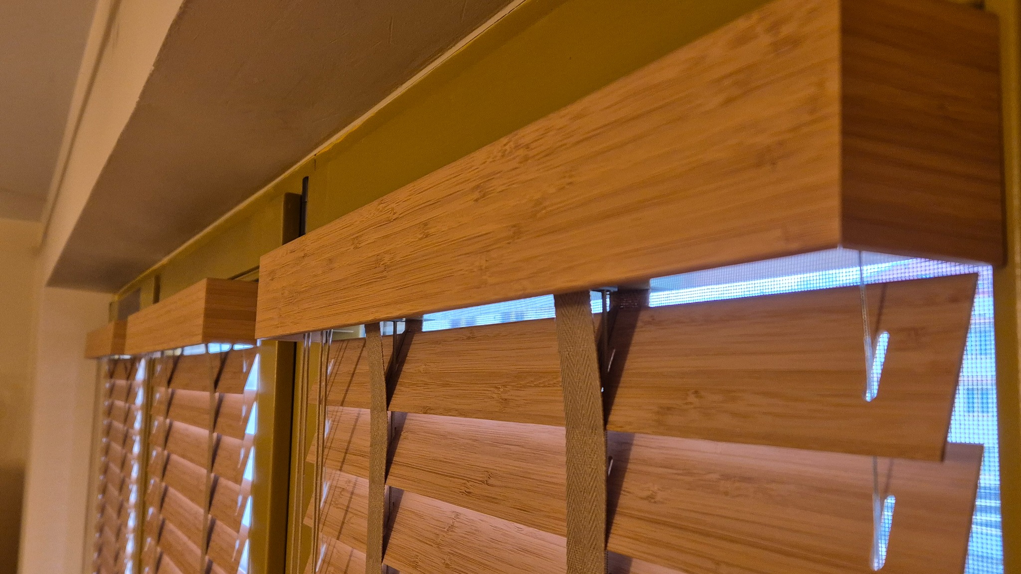 Zamknięte żaluzje drewniane z widoczną siatką moskitiery w oknie. Ujęcie z dołu, podkreślające strukturę drewna i funkcjonalność osłon okiennych.