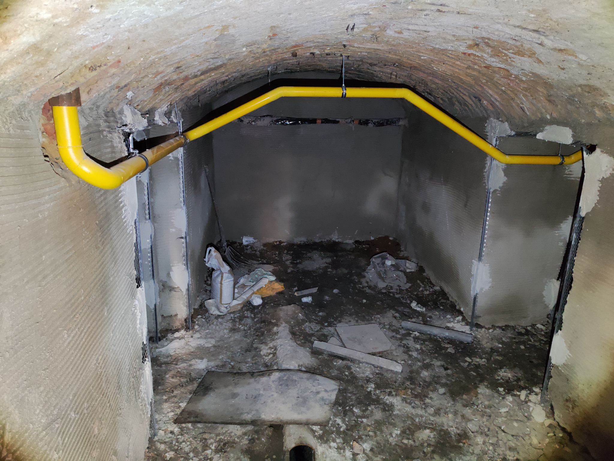 Żółta rura gazowa zamontowana pod sklepieniem piwnicy, widoczne ślady prac remontowych na ścianach i podłodze.