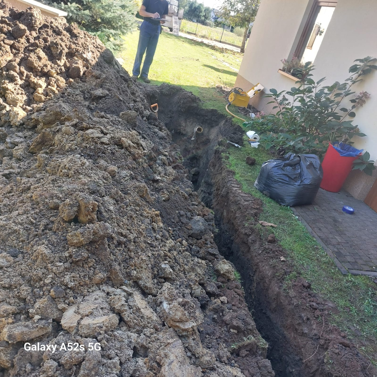 Wykop pod przyłącze wodno-kanalizacyjne w Dąbrowie Górniczej, widoczna rura w ziemi, obok hałda ziemi i pracownik z dokumentacją.