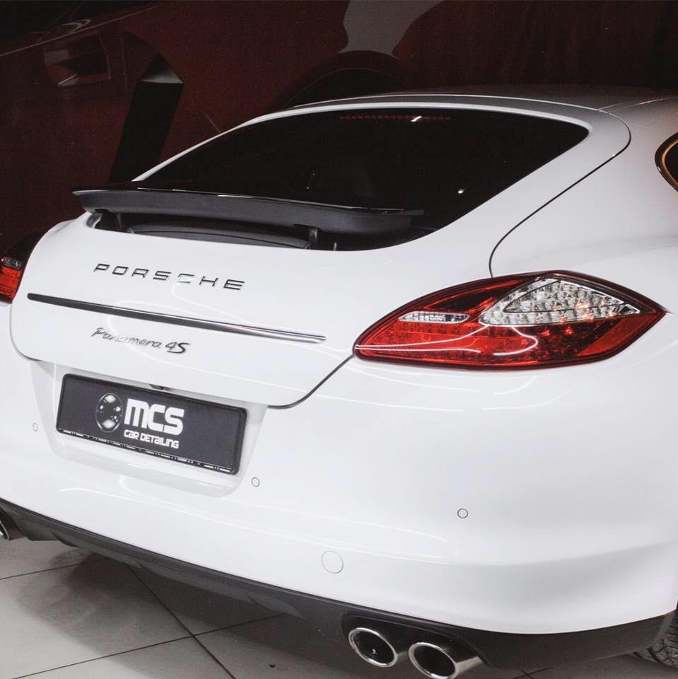 Tył białego Porsche Panamera 4S z przyciemnionymi szybami, widoczne logo firmy detailingowej na tablicy rejestracyjnej.