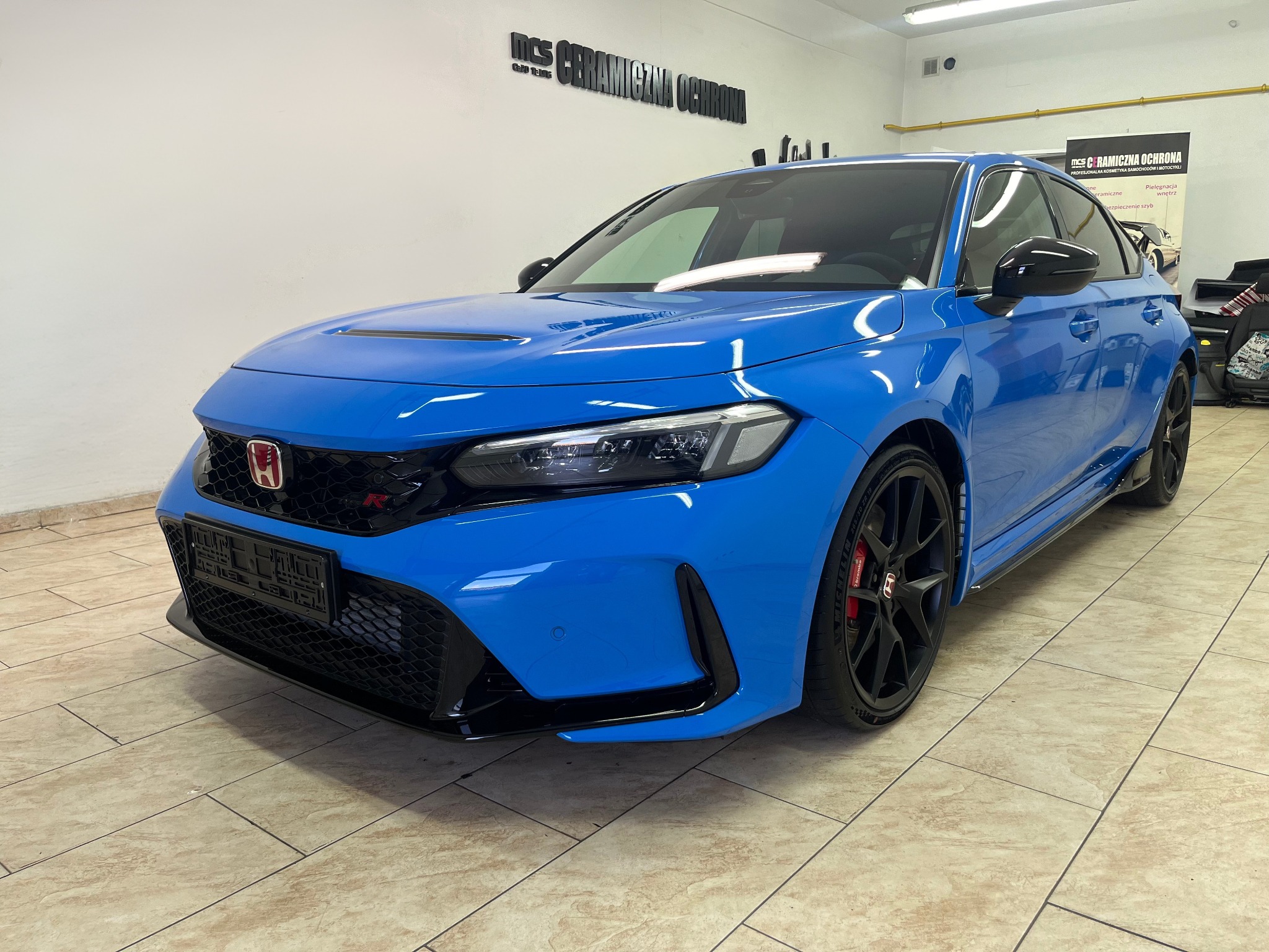 Błękitny samochód Honda Type R po zabiegach pielęgnacyjnych, z widocznym logo firmy zajmującej się ochroną ceramiczną na ścianie warsztatu.