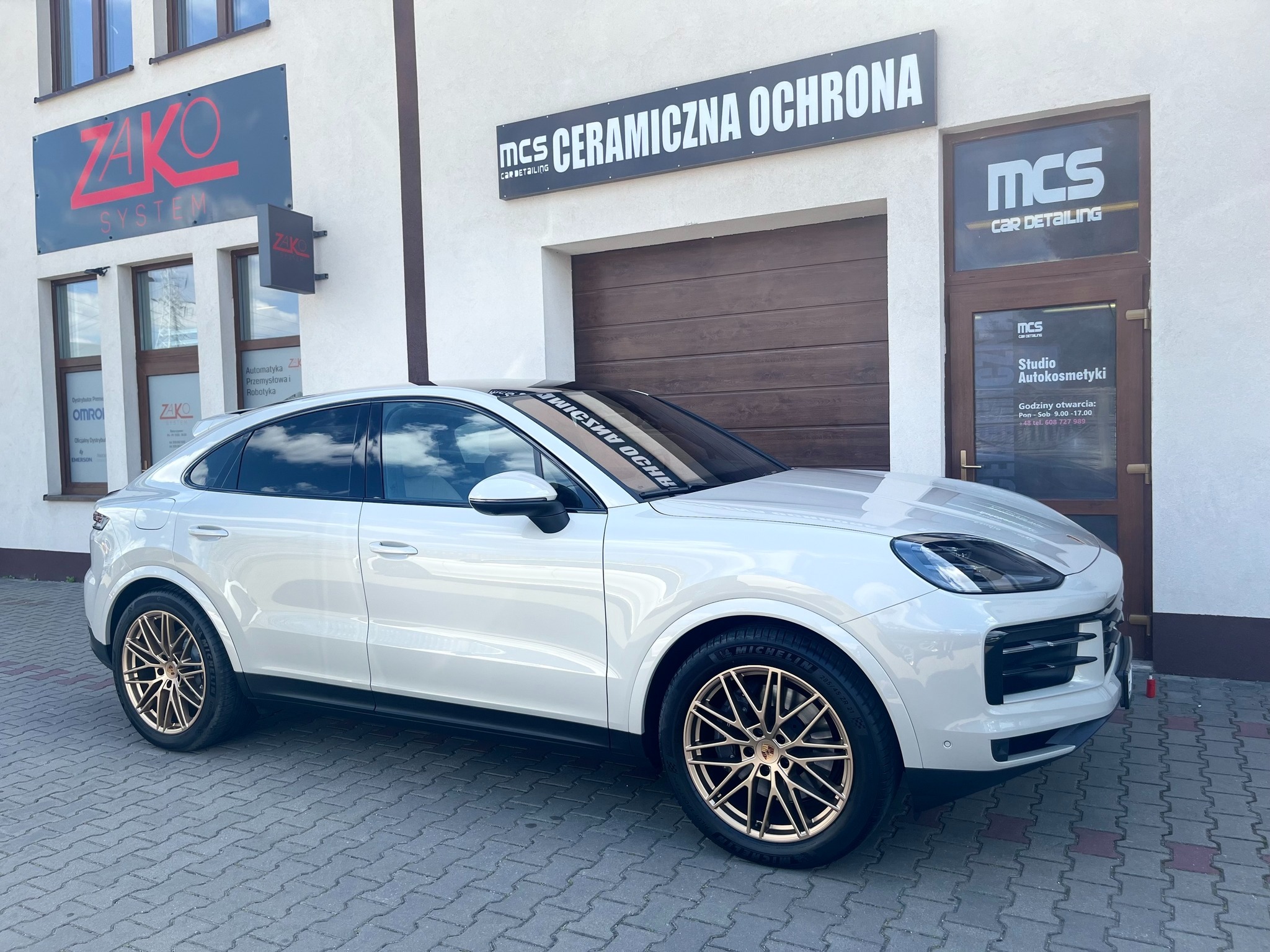 Białe Porsche Cayenne po zabiegach auto detailingu, zaparkowane przed studiem MCS Car Detailing. Widoczne złote felgi i połysk karoserii.