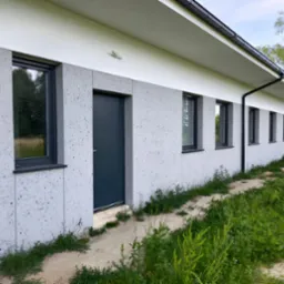 Elewacja budynku wykończona panelami imitującymi lastryko, antracytowa stolarka okienna i drzwiowa, widoczne rynny spustowe.