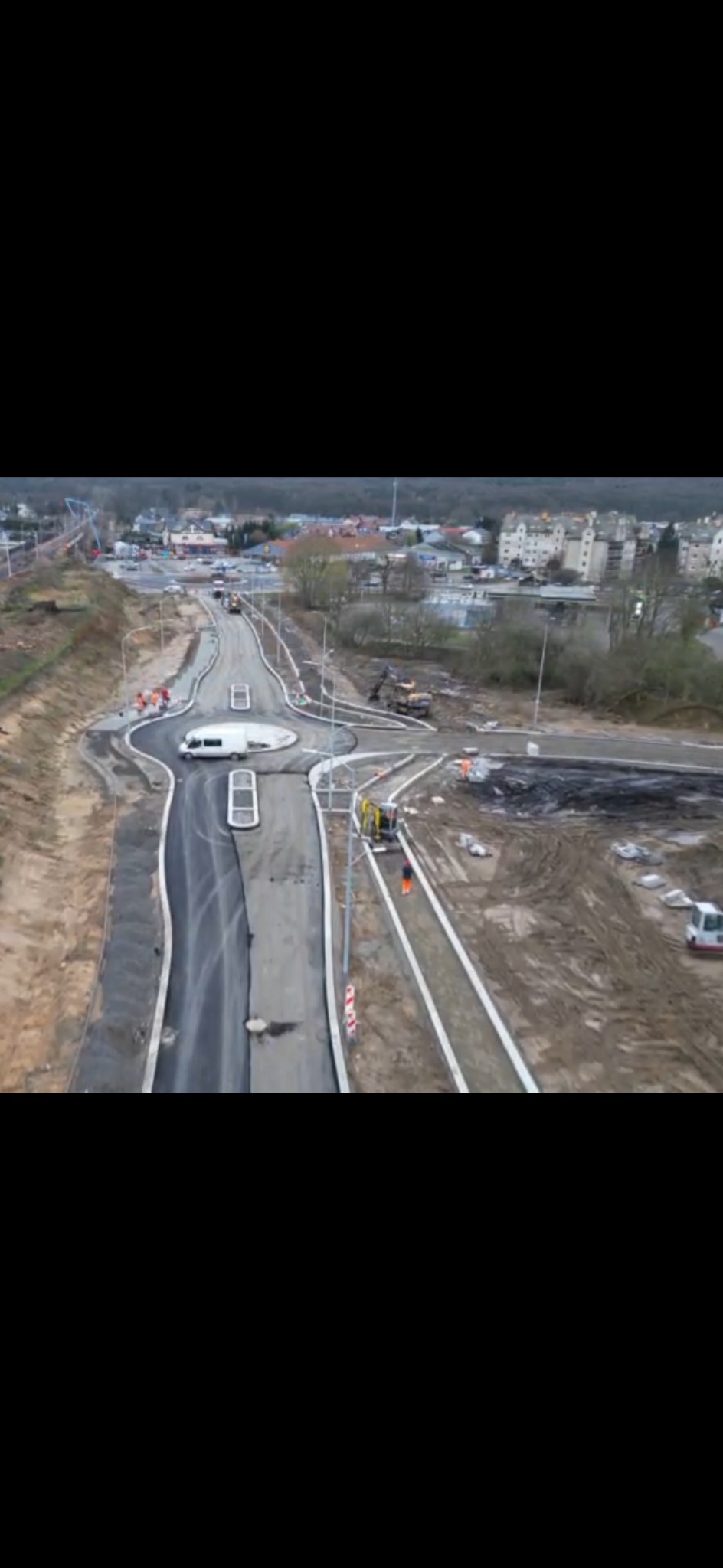Widok z góry na budowę ronda w Policach, z widocznymi maszynami budowlanymi i pracownikami w odblaskowych ubraniach, w tle zabudowa miejska.