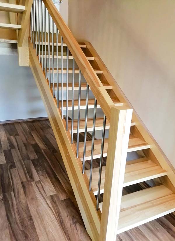Jasne, drewniane schody z metalowymi balustradami, widok z dołu, na podłodze panele imitujące drewno.
