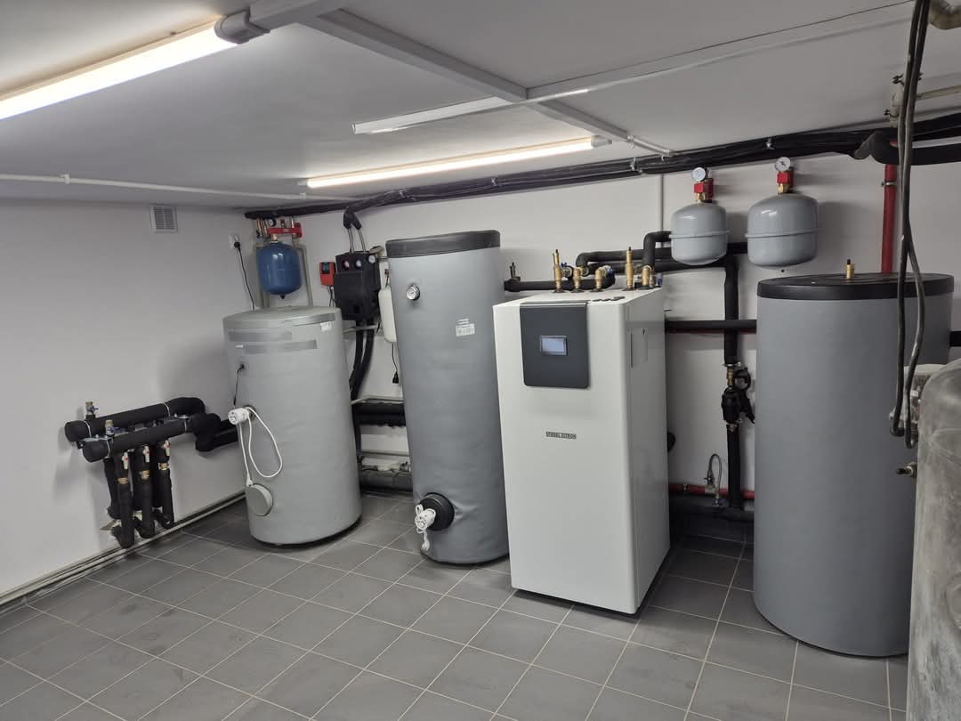 Kompletna instalacja kotłowni z pompą ciepła Stiebel Eltron, zbiornikami buforowymi i osprzętem hydraulicznym w pomieszczeniu technicznym wyłożonym szarą terakotą.