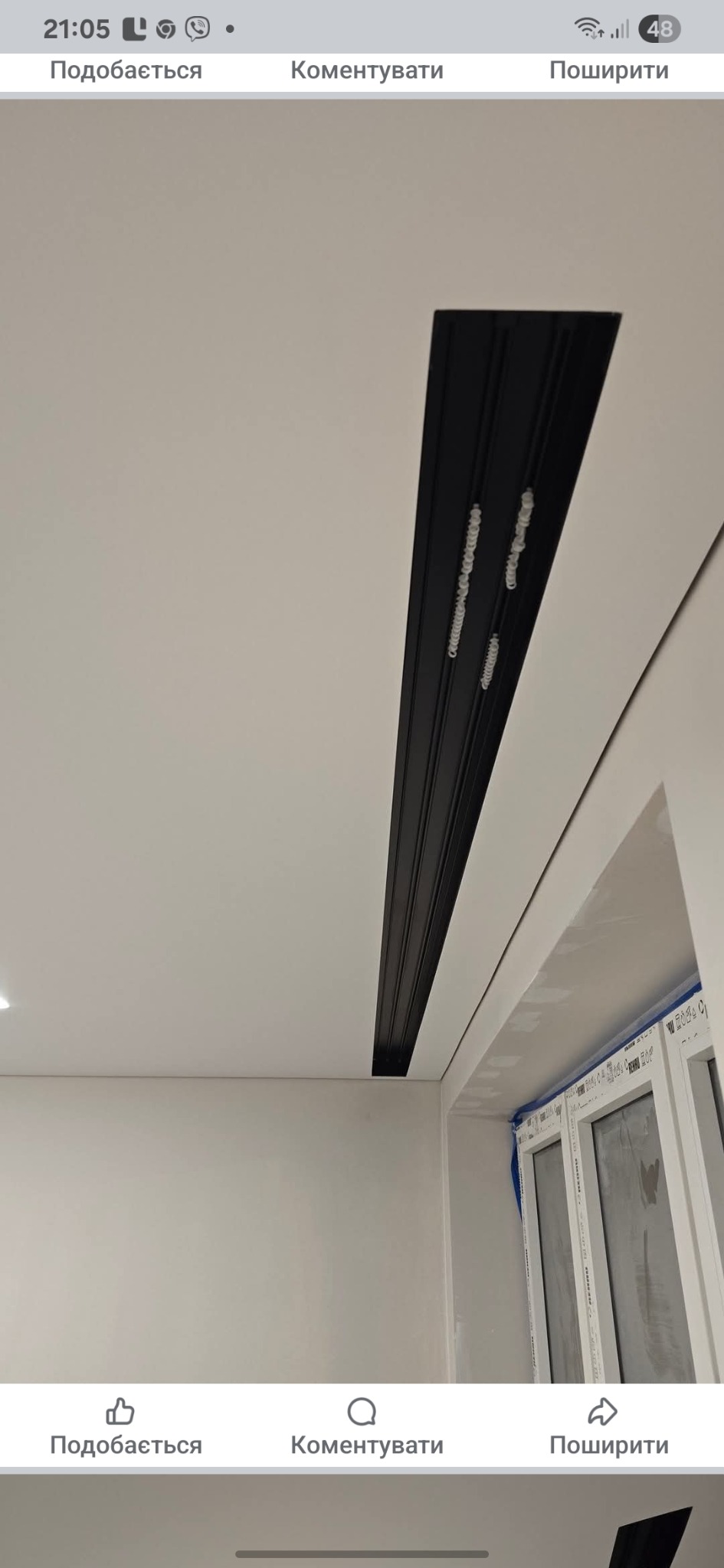 Zamontowany czarny profil sufitowy z widocznymi elementami mocującymi, białe ściany i okno w tle. Detal wykończenia wnętrza, nowoczesny design.