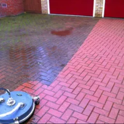 Częściowo wyczyszczona kostka brukowa przed garażem z użyciem myjki ciśnieniowej, widoczny kontrast między brudną i czystą powierzchnią.