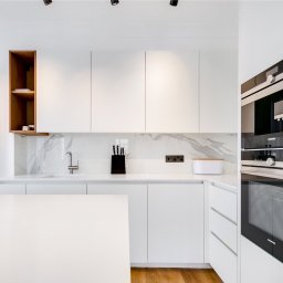 W.E - Nowoczesna, minimalistyczna kuchnia z białymi szafkami, marmurowym blatem i drewnianymi akcentami. Widoczny piekarnik Siemens i grzejnik dekoracyjny.