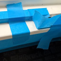 EUROBUD-SK Serhii Kasianchuk - Biała rama okienna zabezpieczona niebieską taśmą malarską, przygotowana do malowania. Widoczny fragment podłoża z napisem 'illbruck'.