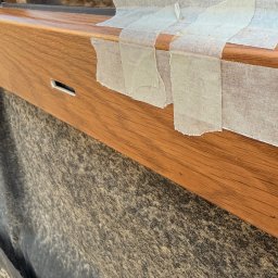 EUROBUD-SK Serhii Kasianchuk - Drewniane okno zabezpieczone taśmą malarską, gotowe do obróbki. Widoczny fragment okna i materiał zabezpieczający elewację. Ujęcie z bliska, detale wykończenia.