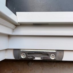 EUROBUD-SK Serhii Kasianchuk - Szczegółowe ujęcie mechanizmu blokującego w białej ramie okiennej z widocznymi śrubami i strzałką kierunkową na metalowym elemencie, ukazujące precyzję montażu.