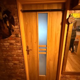 EUROBUD-SK Serhii Kasianchuk - Drewniane drzwi wewnętrzne z przeszkleniem, zamontowane w ścianie z czerwonej cegły. Widoczne detale wykończenia i odbicie w lustrze obok.