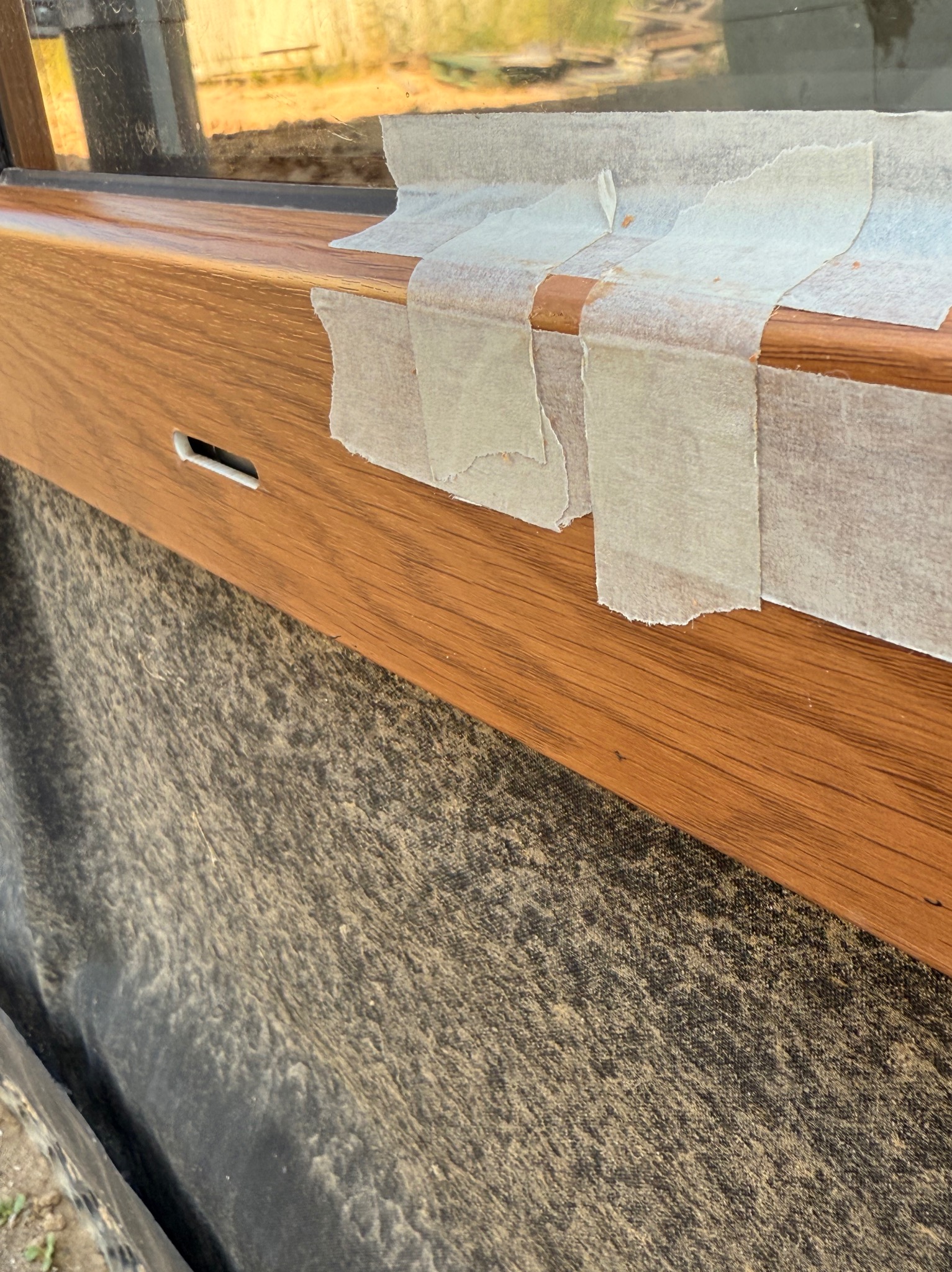 Drewniane okno zabezpieczone taśmą malarską, gotowe do obróbki. Widoczny fragment okna i materiał zabezpieczający elewację. Ujęcie z bliska, detale wykończenia.