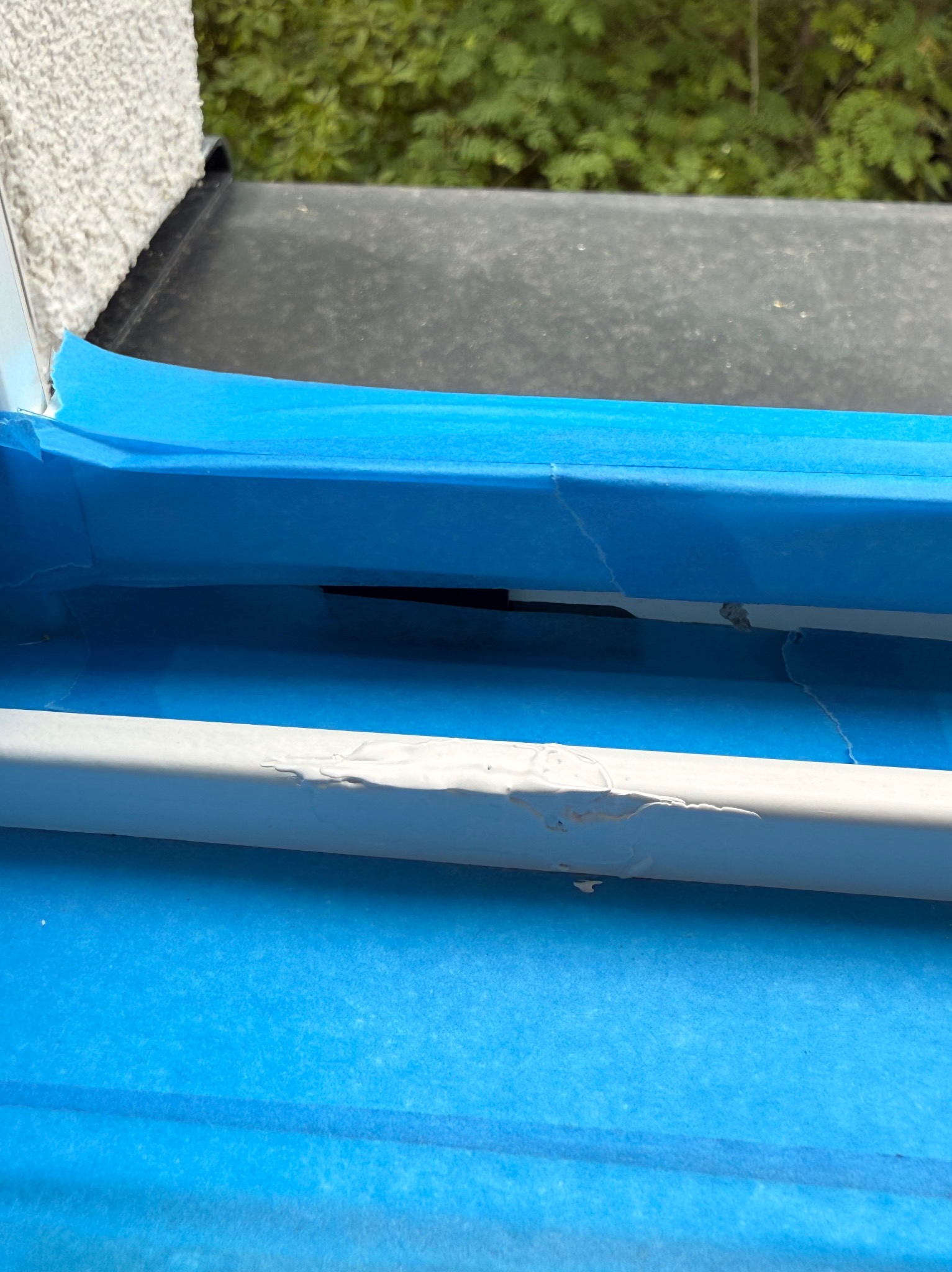 Fragment odnowionego balkonu z zabezpieczonymi taśmą elementami, świeżo pomalowana barierka w kolorze szarym. Widoczne niedoskonałości malowania.