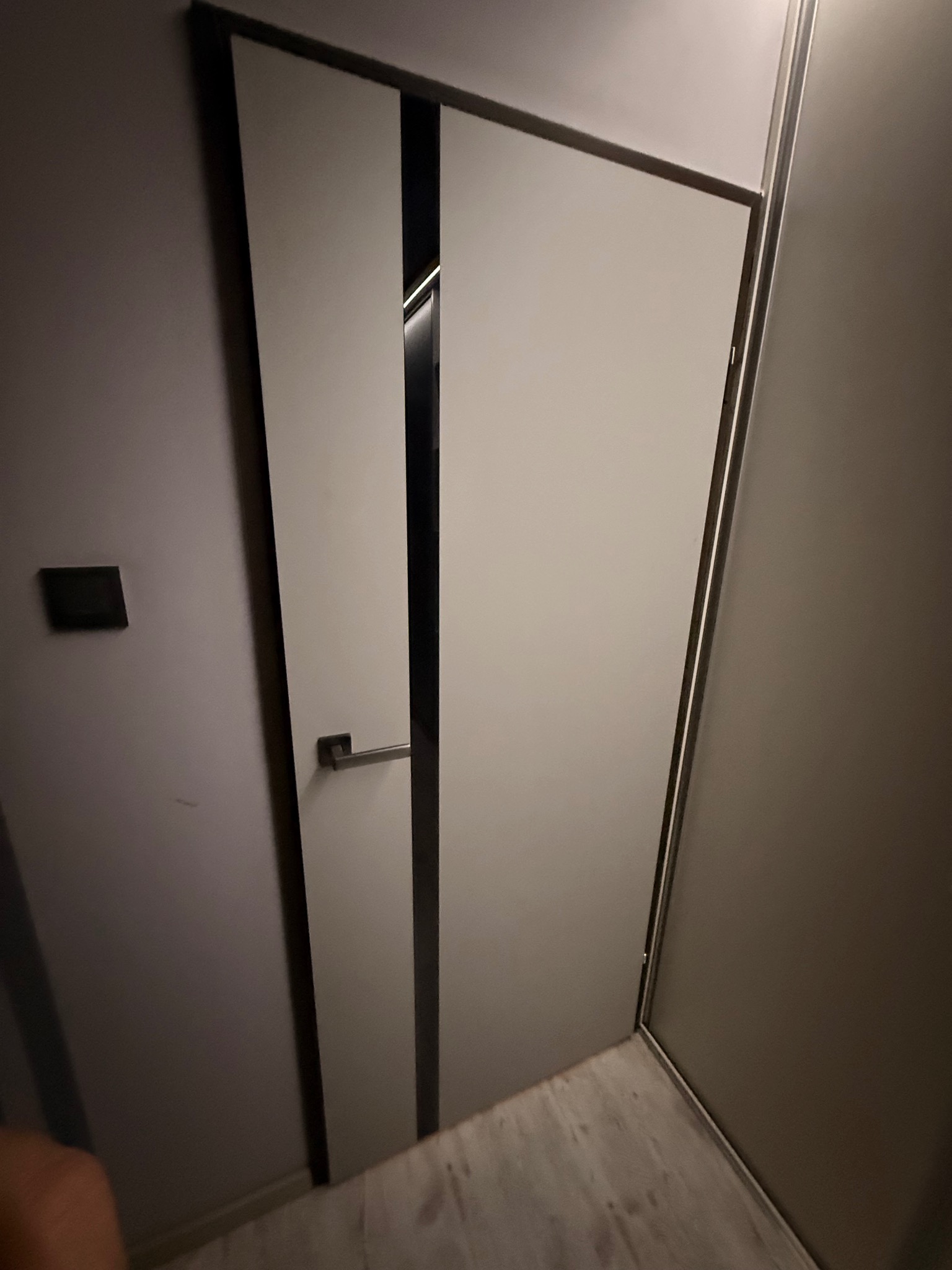 Zamknięte, nowoczesne drzwi wewnętrzne z metalową klamką i czarnymi, pionowymi akcentami, widoczne z perspektywy lekko z góry, w jasnym wnętrzu.