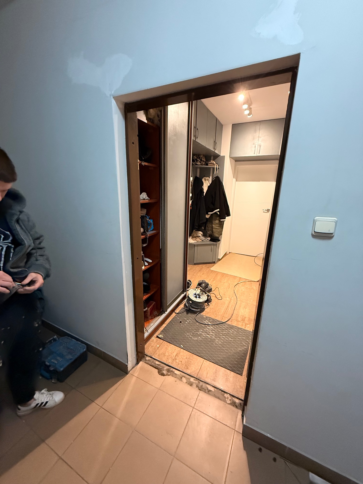 Wnętrze mieszkania w trakcie prac wykończeniowych: widoczne ślady szpachlowania na ścianie, przesuwne drzwi do garderoby i narzędzia. Ujęcie z perspektywy podłogi.