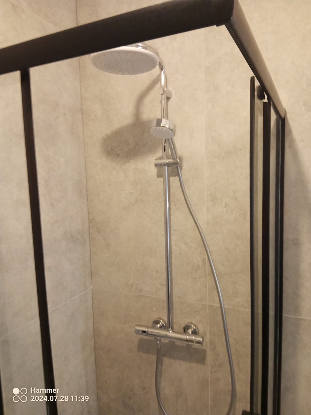 Nowoczesna kabina prysznicowa z deszczownicą i termostatem, wykończona płytkami imitującymi kamień, z czarną ramą.