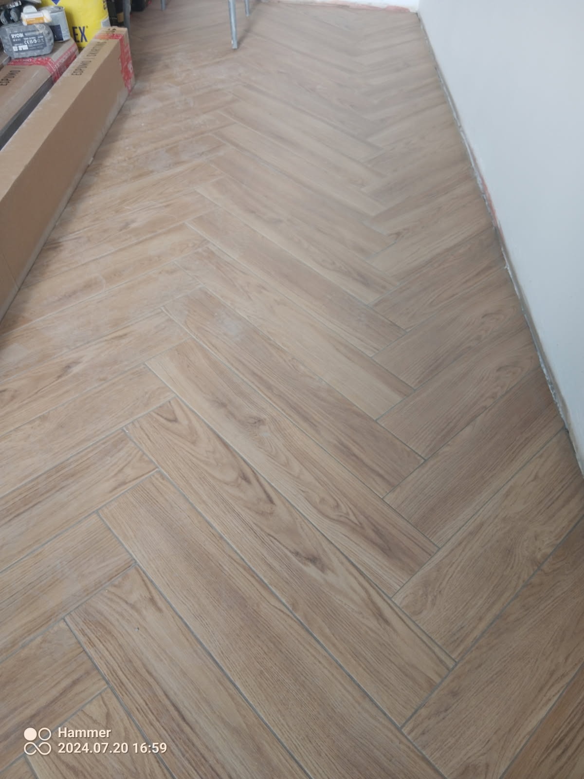 Ułożona podłoga z paneli imitujących drewno w jodełkę, widoczne kartony z panelami przy ścianie.