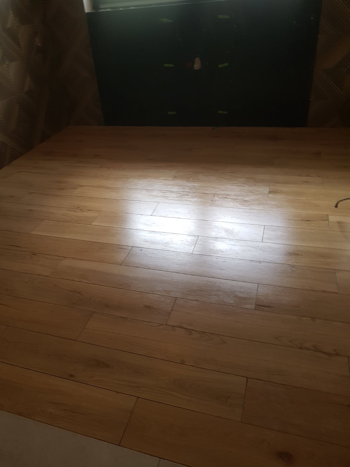 Ułożona podłoga z paneli imitujących drewno, widoczne ślady po taśmie malarskiej na ścianie w tle.