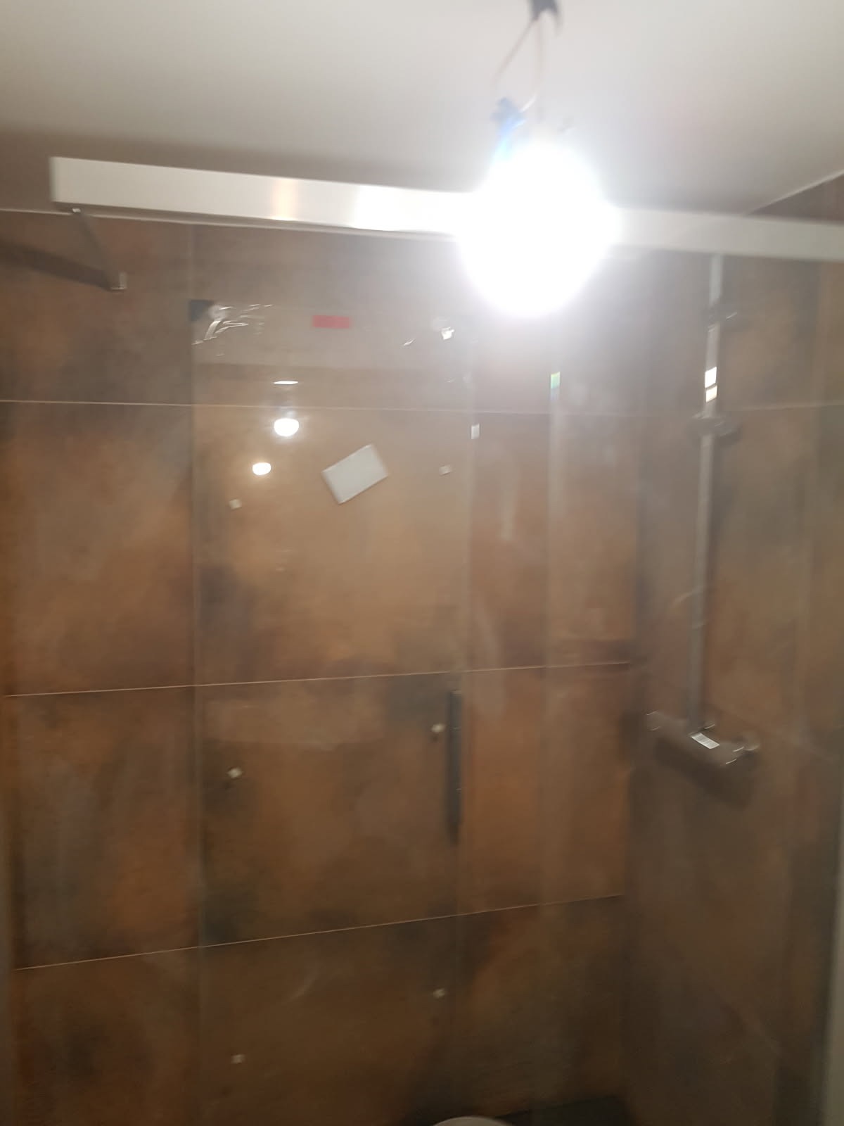 Kabina prysznicowa z brązowymi płytkami w łazience w Łodzi, widoczny panel prysznicowy i biała naklejka na szkle.