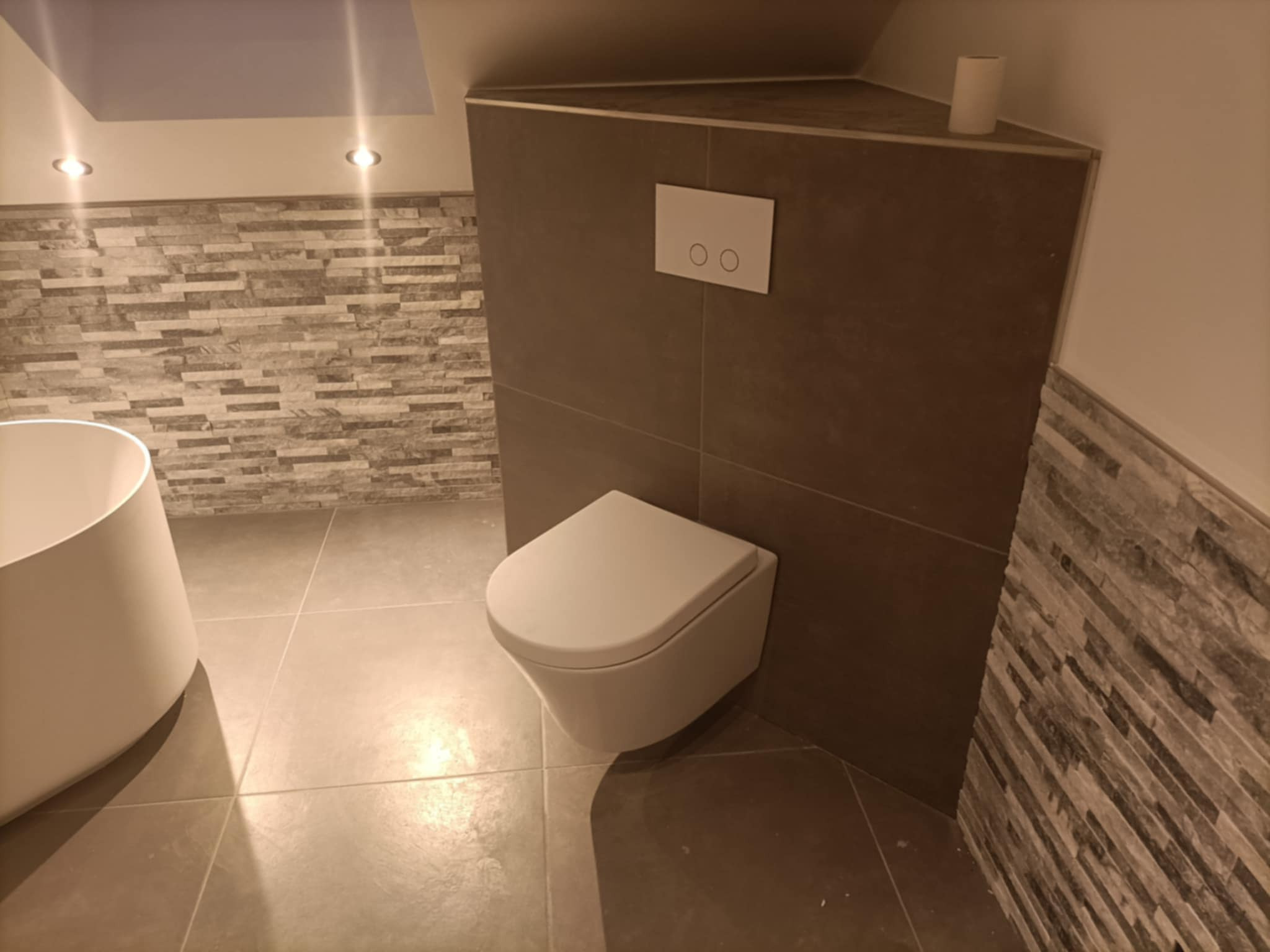 Nowoczesna łazienka z podwieszaną toaletą, szarą mozaiką na ścianach i podświetleniem sufitowym, prezentująca wykończenie w neutralnej kolorystyce.