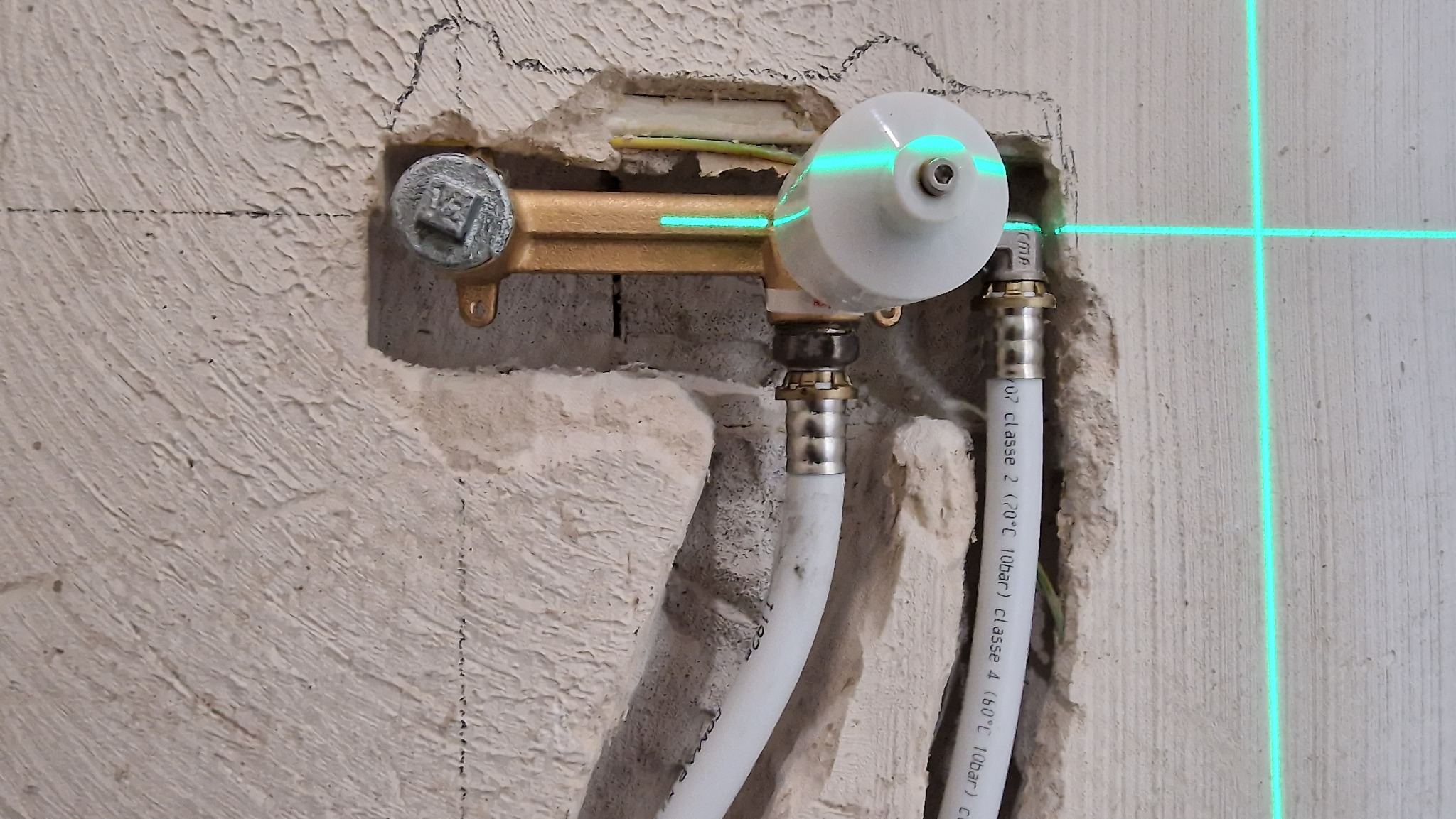 Mosiężna bateria podtynkowa zamontowana w surowej ścianie, poziomowana laserowo, widoczne białe rury doprowadzające wodę.