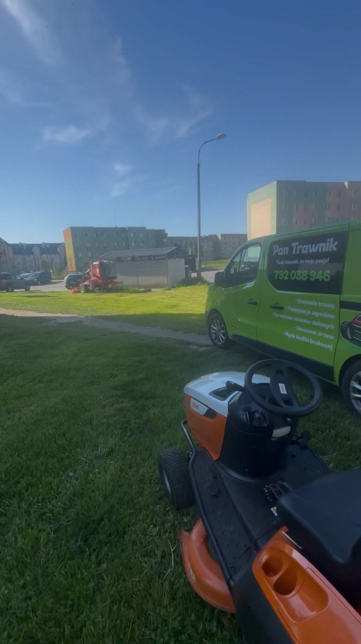 Traktorek-kosiarka Stihl na trawniku, w tle budynki i bus 'Pan Trawnik' z ofertą: koszenie, pielęgnacja, sprzątanie terenów zielonych, usuwanie drzew, mycie kostki.