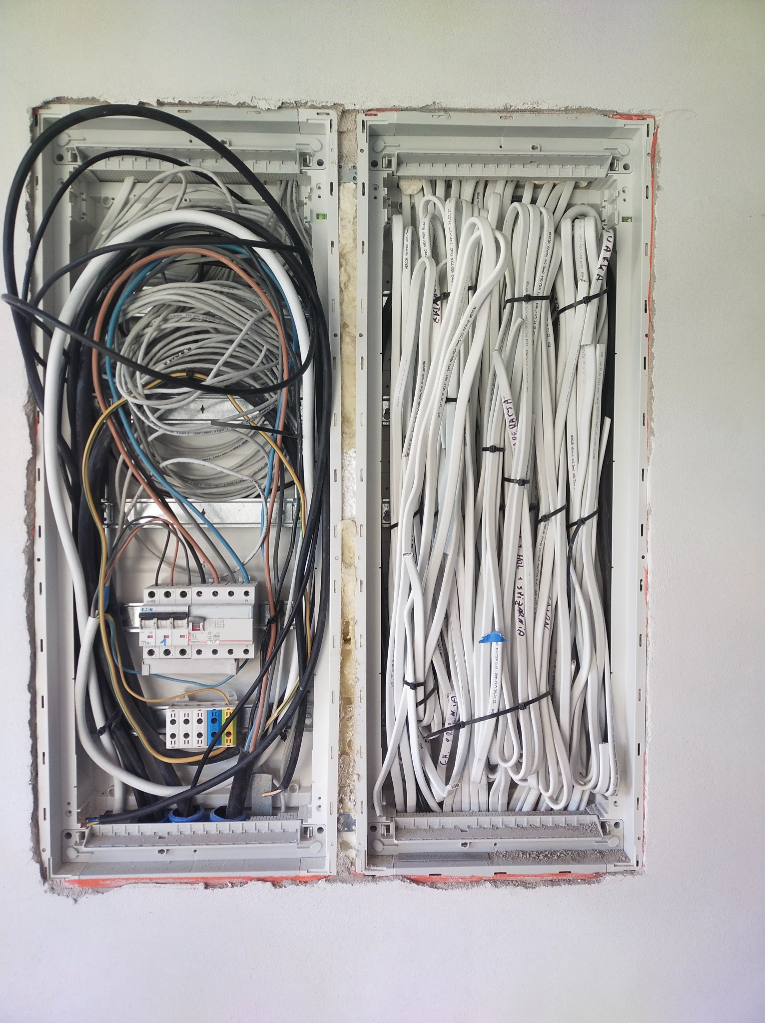 Rozdzielnica elektryczna w trakcie montażu, widoczne kable różnego rodzaju w dwóch skrzynkach, część kabli uporządkowana i spięta opaskami, część luźno ułożona, na kablach widoczne napisy...