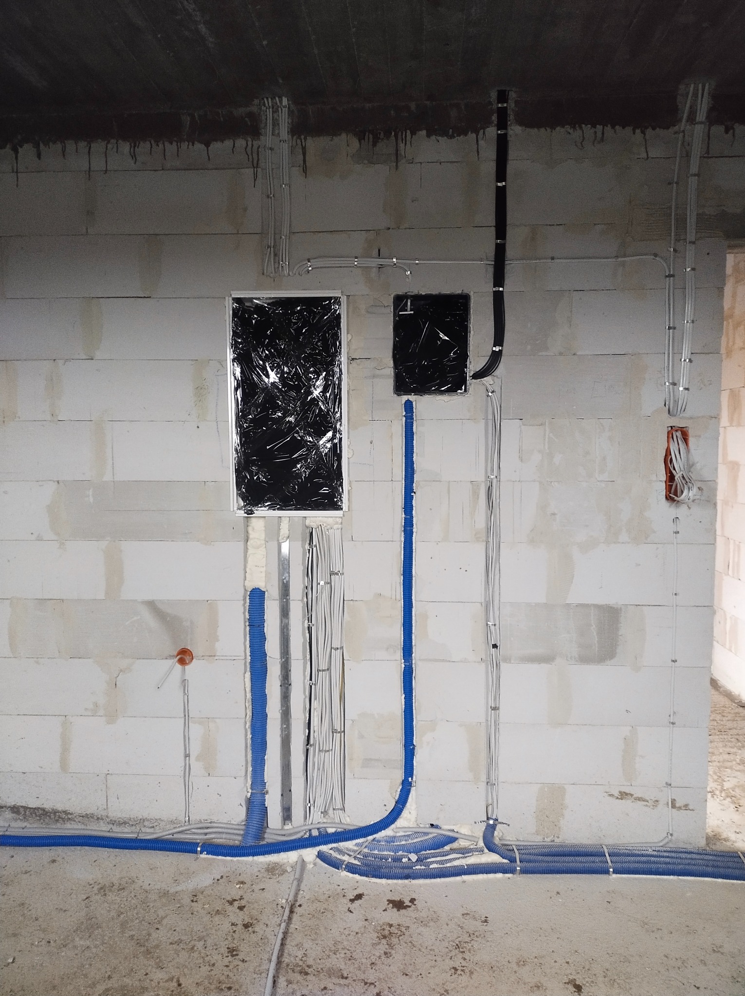 Surowy stan instalacji elektrycznej w budynku: kable w peszlach i rurkach mocowane do ściany z betonu komórkowego, otwory na puszki zabezpieczone folią.