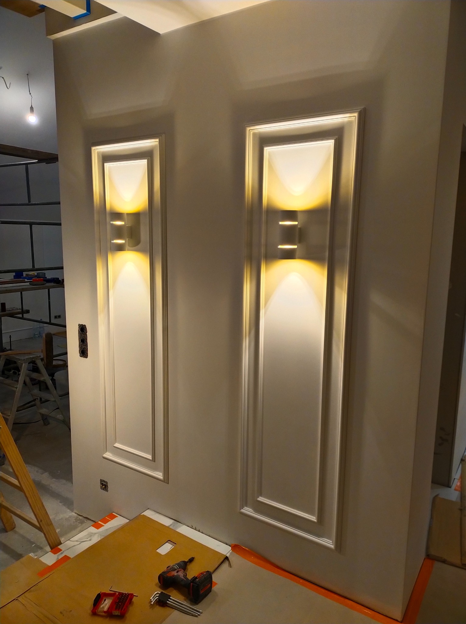 Dwa ozdobne panele ścienne z wbudowanym nowoczesnym oświetleniem LED, widoczne narzędzia i osłony podłogowe podczas montażu.