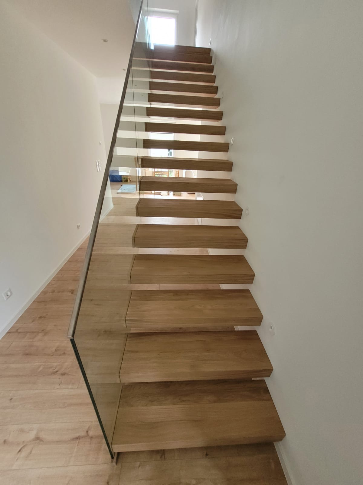 Nowoczesne, drewniane schody z balustradą ze szkła w domu w Żabiej Woli, oświetlone naturalnym światłem z okna na górze.