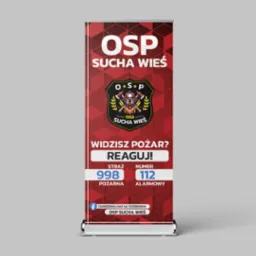 Roll-up reklamowy z logo i hasłem OSP Sucha Wieś, informujący o numerach alarmowych straży pożarnej, z odnośnikiem do Facebooka.