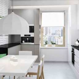 Max bud - Jasna kuchnia z białymi frontami szafek, czarnym blatem, szarą tapicerowaną ławą i stołem, widok na miasto z okna.