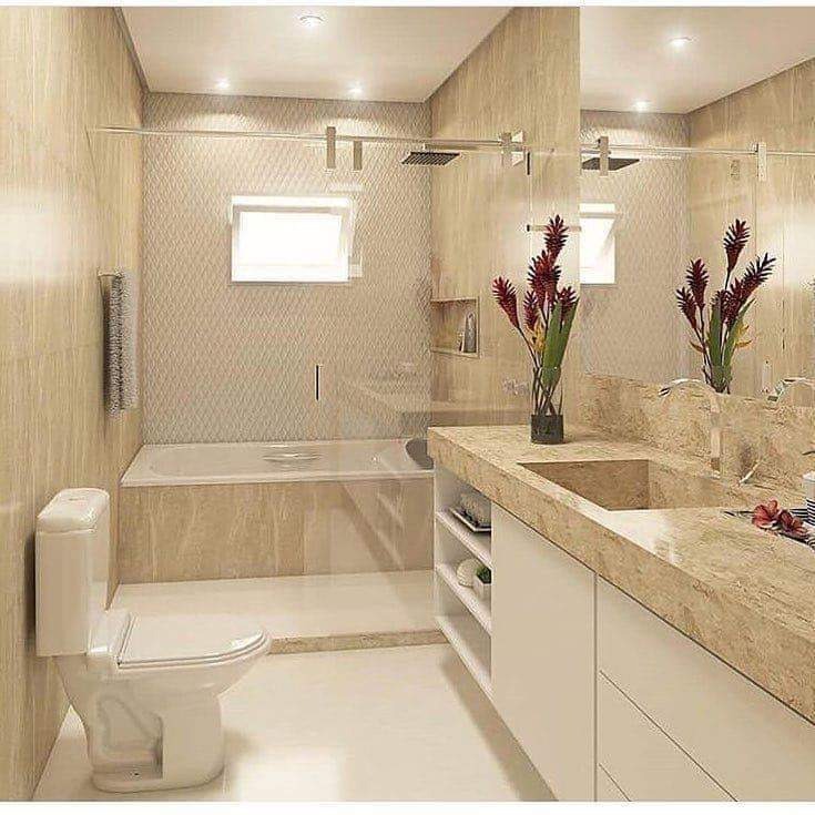 Nowoczesna łazienka z beżowymi płytkami, szklaną kabiną prysznicową, białym WC i umywalką z blatem imitującym marmur, uzupełniona o dekoracyjne kwiaty w wazonie.