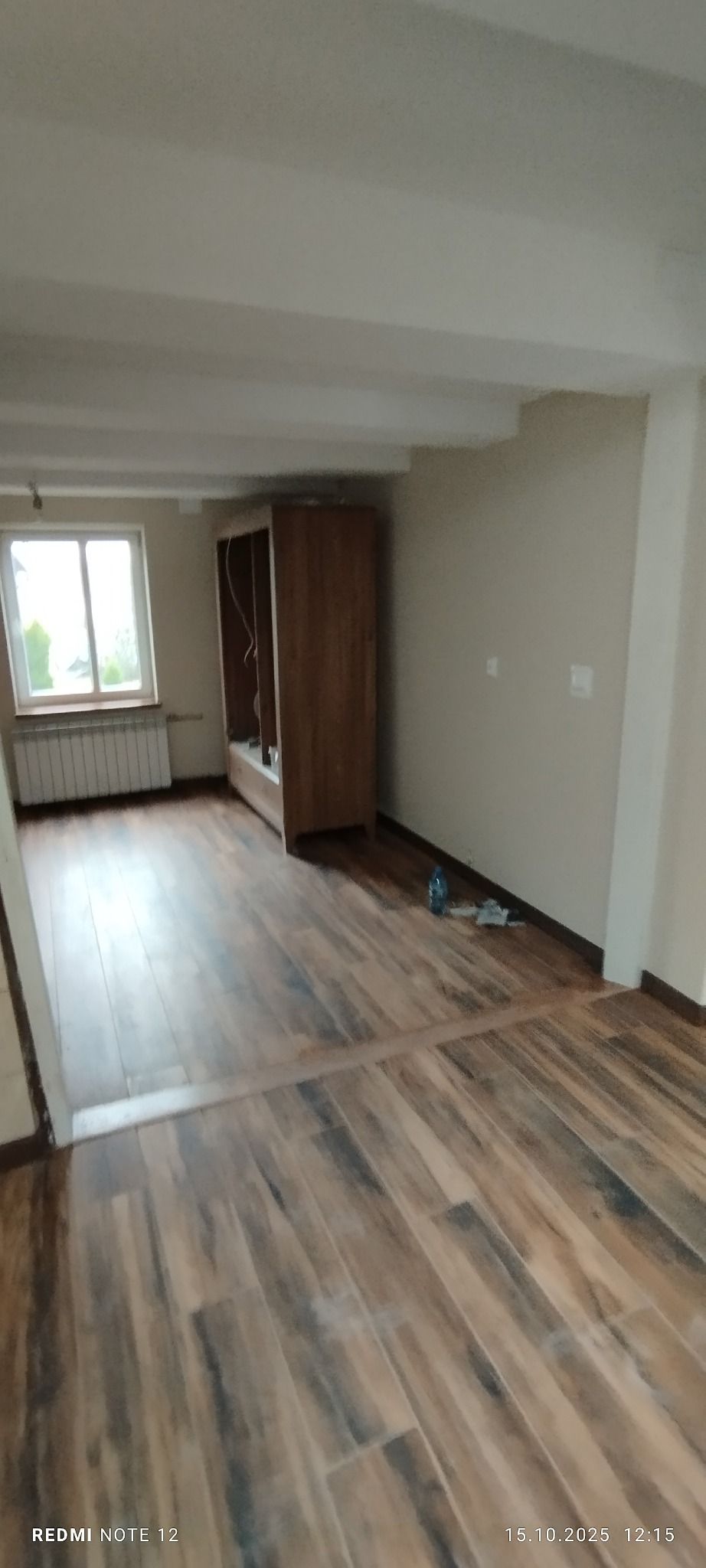 Ułożone panele podłogowe imitujące drewno w jasnym pokoju w Radomyślu nad Sanem. Widoczny fragment ściany, okno i niedokończona szafa.