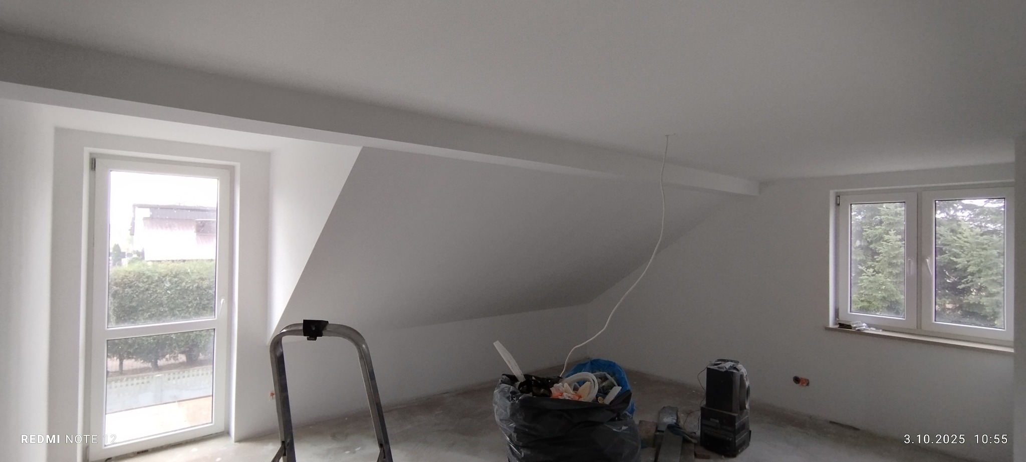 Pomalowane na biało poddasze ze skosami, widoczne okna, drabina malarska i worki z odpadami po remoncie. Świeżo po malowaniu.