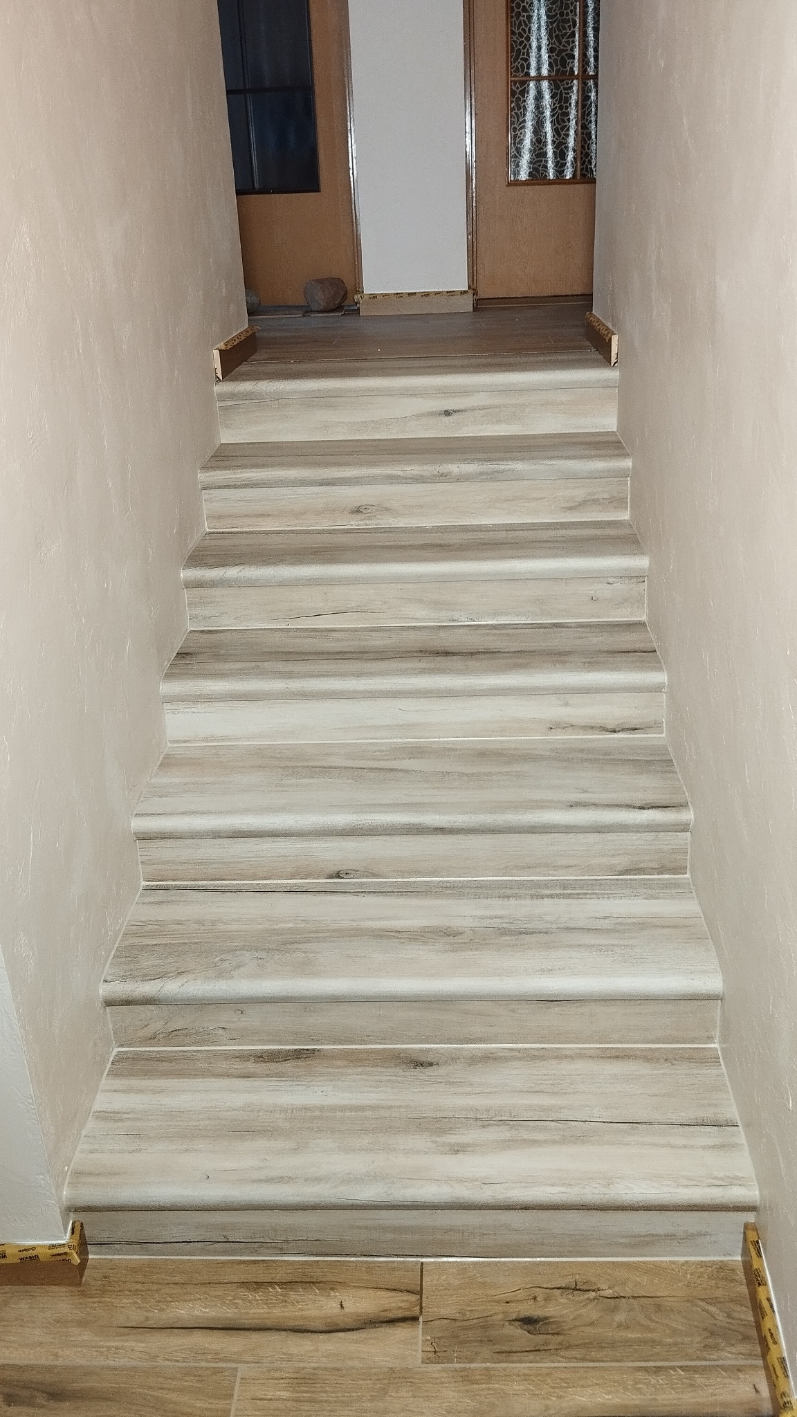 Wykończone schody z panelami imitującymi drewno, prowadzące do góry. Ściany w jasnym odcieniu beżu. Widoczne detale wykończenia i faktura paneli.