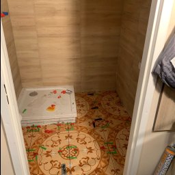 Szymon Lipka Usługi Budowlane - Łazienka w trakcie remontu: układanie wzorzystych płytek podłogowych, płytki imitujące drewno na ścianach, widoczne narzędzia i system poziomowania płytek.