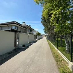 Malowanie elewacji ogrodzenia posesji nowoczesnego domu jednorodzinnego przy użyciu wałka, widok z ulicy w słoneczny dzień.