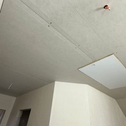 Szymon Lipka Usługi Budowlane - Sufit podwieszany z płyt gipsowo-kartonowych, widoczne łączenia, otwór rewizyjny z metalowym haczykiem oraz wystający kabel z instalacji elektrycznej.