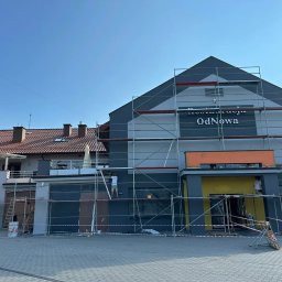 Szymon Lipka Usługi Budowlane - Dwukondygnacyjny budynek z napisem 'Restauracja OdNowa' na elewacji, otoczony rusztowaniami, dwóch pracowników w trakcie prac malarskich, widoczne puszki z farbą i drabina.