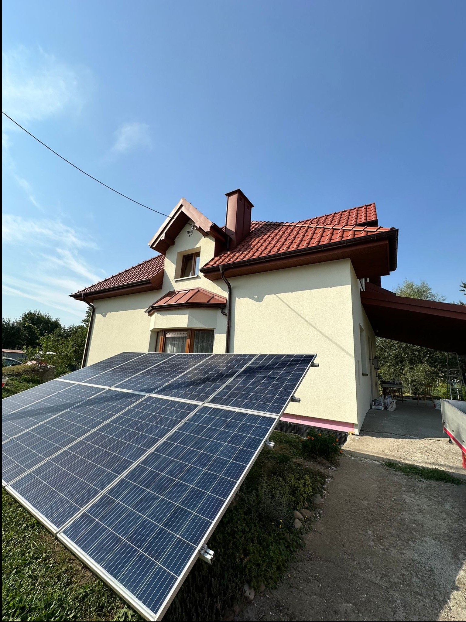 Jasny dom jednorodzinny z czerwoną dachówką i panelami słonecznymi zamontowanymi na trawniku, widok z dołu w słoneczny dzień.