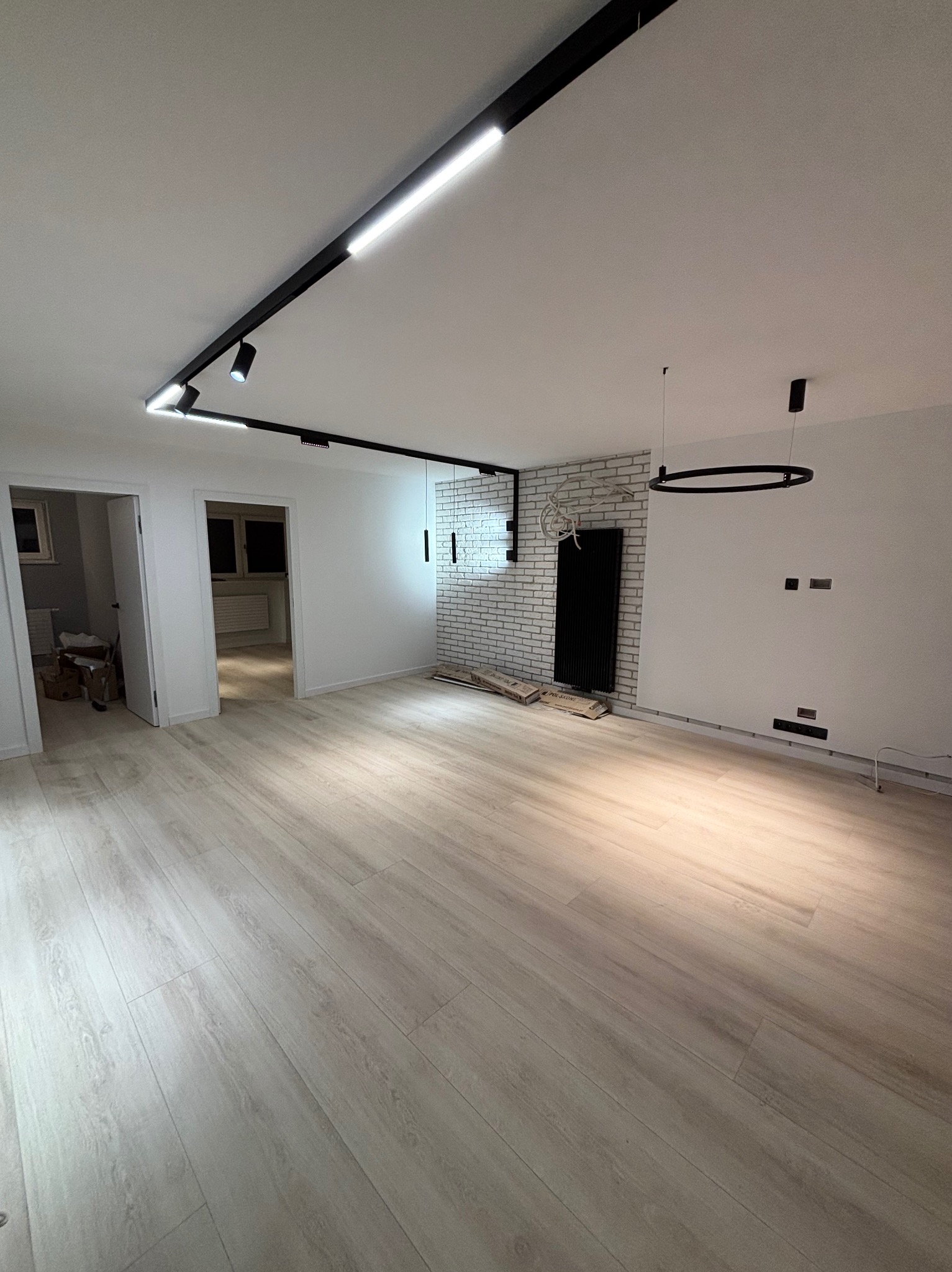 Jasne, przestronne wnętrze po remoncie z panelami podłogowymi, oświetleniem szynowym i dekoracyjną ścianą z białej cegły.