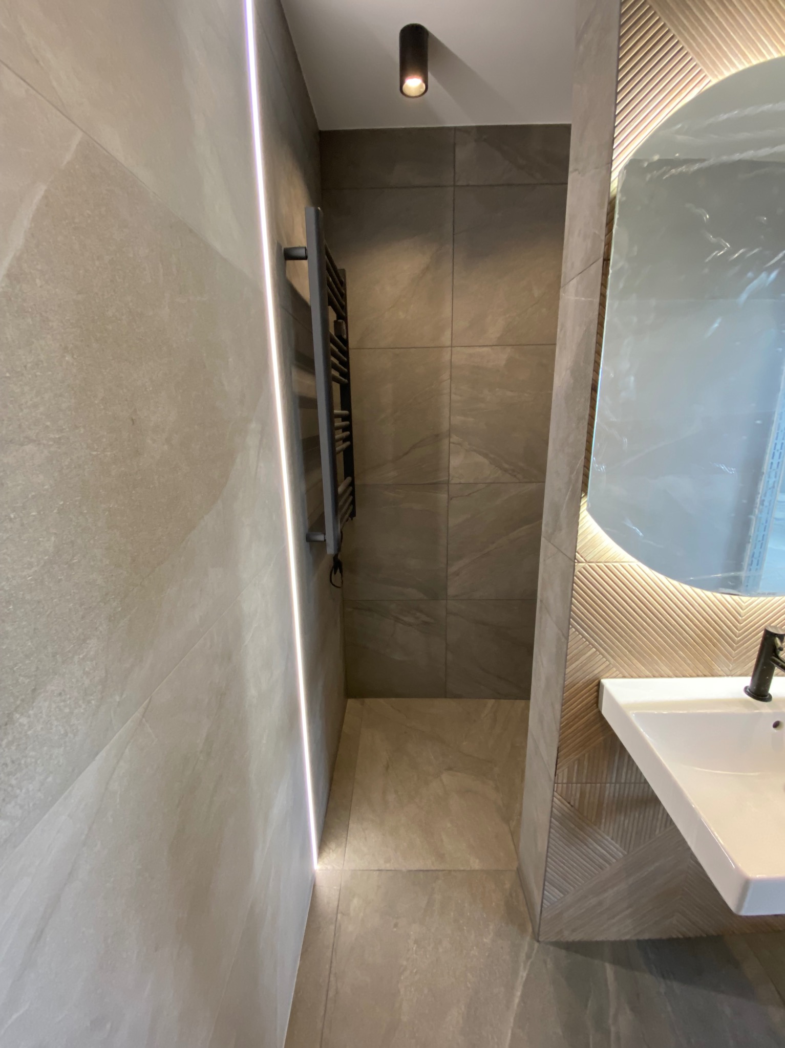 Nowoczesna łazienka w odcieniach szarości z podświetlanym lustrem i grzejnikiem drabinkowym, widok z perspektywy podłogi.