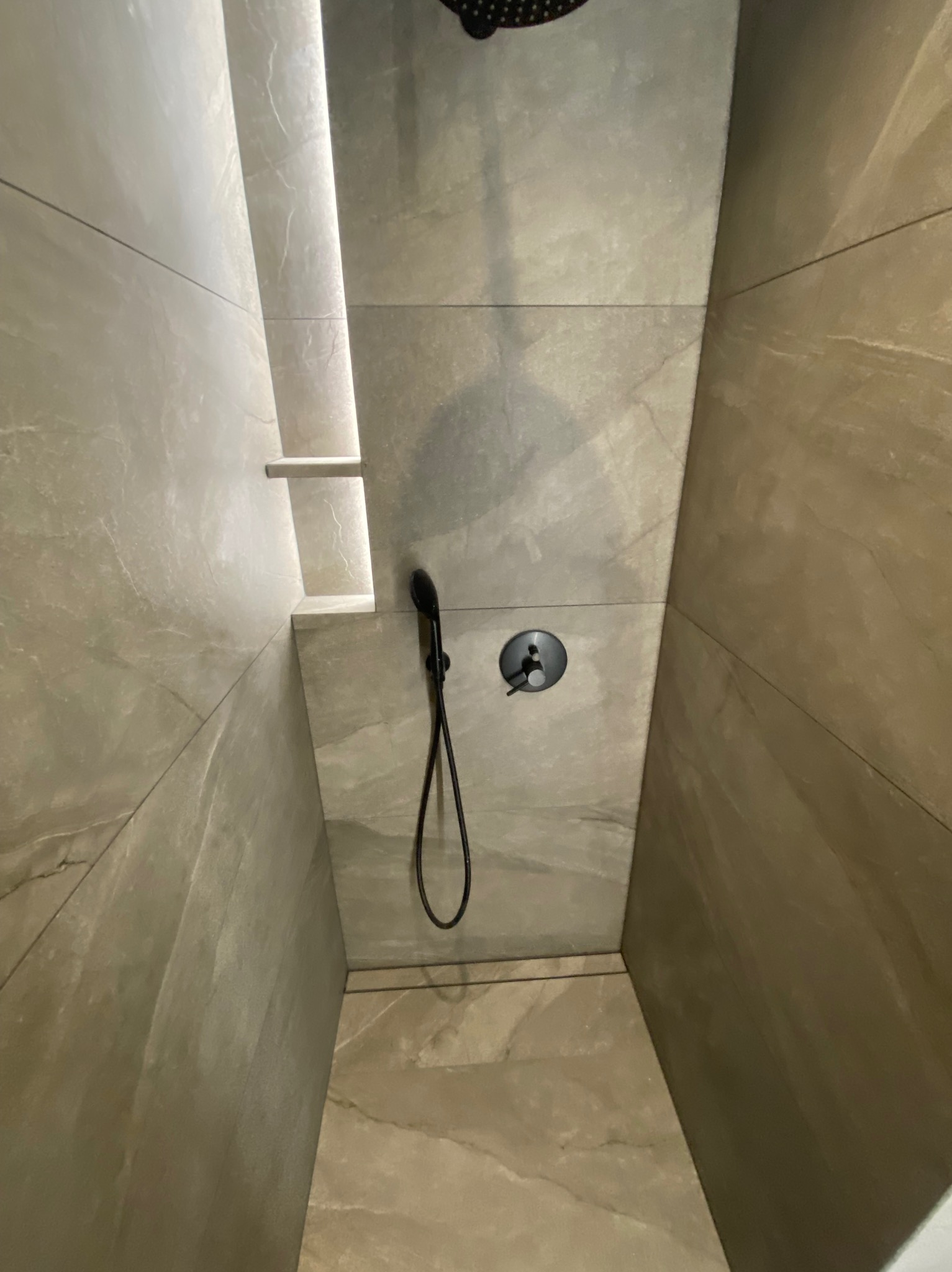 Nowoczesna kabina prysznicowa z szarymi płytkami imitującymi marmur, czarną armaturą i oświetleniem LED wzdłuż ściany.